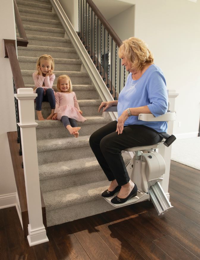 senior woman sitting on stair lift and smiling at grandchildren sitting on the stairs