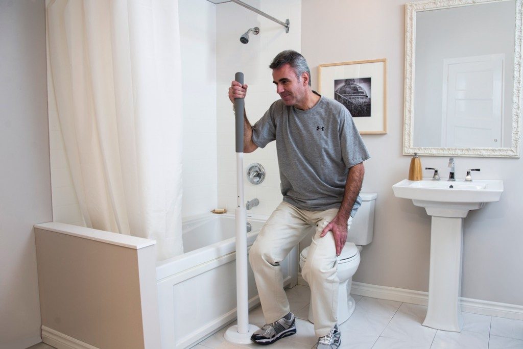 man using super pole to safely get off of toilet in bathroom in his home