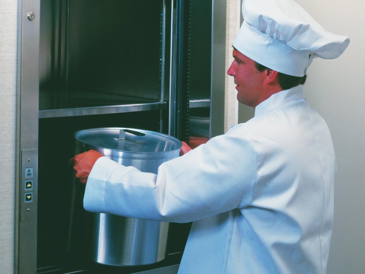 A chef putting a large pot into a commercial dumbwaiter