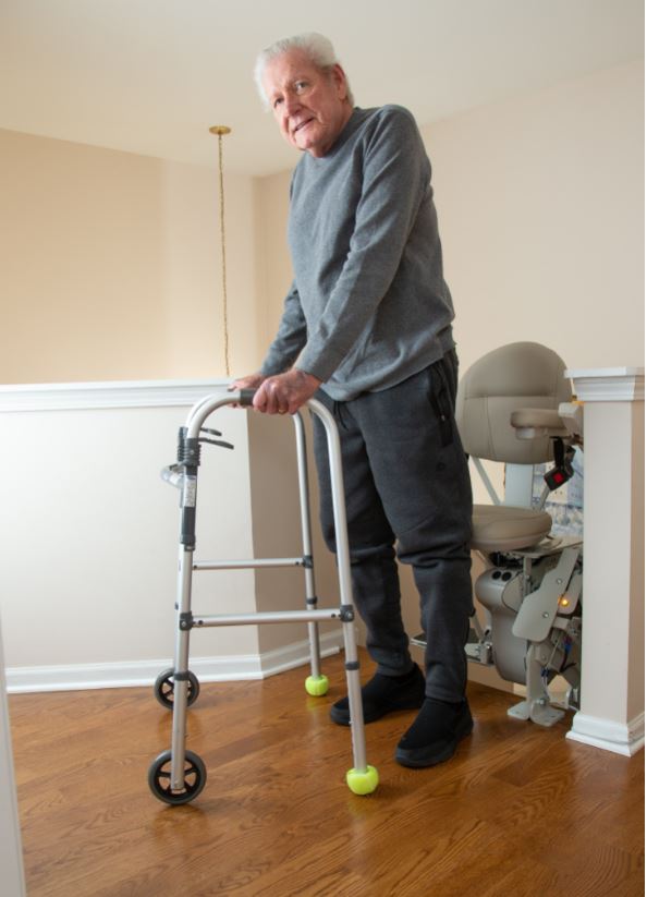 disabled man using walker to safely exit stair lift at top of staircase